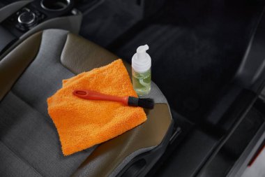 Ön yolcu koltuğunda dezenfektan sprey şişesinde fırça havlusu ve deterjan var. Yüksek açılı yakın çekim. Araba temizleme kavramı