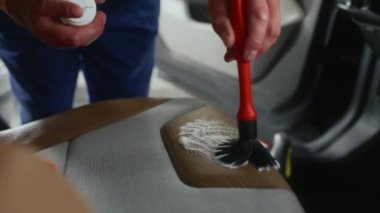 Araba temizleme işçisi arabanın içini deterjan köpüğü ve fırçayla temizliyor. Araba temizleme ve temizlik servisi
