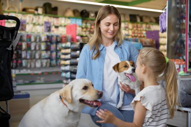Mutlu anne ve kız veteriner dükkanında küçük ve büyük köpek arasında seçim yapıyorlar. Ev için yeni evcil hayvan satın almak