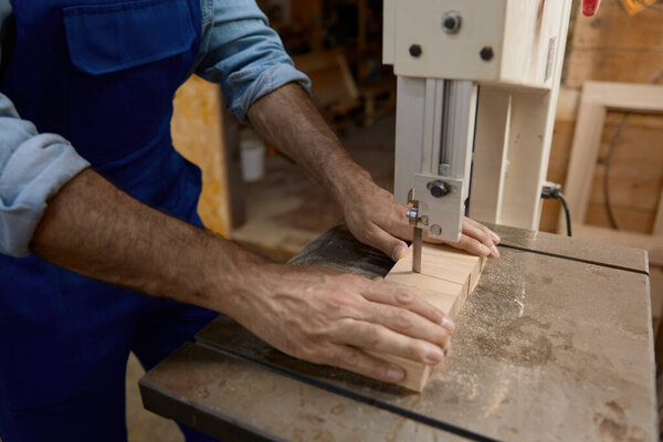 Carpentry shop worker processing woods at stationary electric jigsaw. Professional job occupation at furniture production manufactory