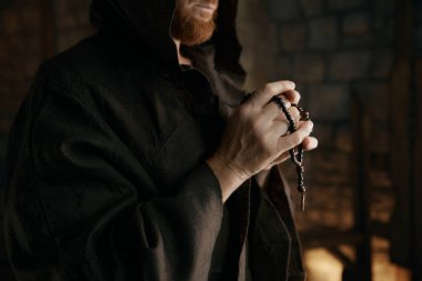 Keşişin yakın çekimlerinde dua ederken ya da tespih boncukları ellerindeyken ortaçağ manastırının iç kısımlarında dururken.