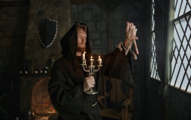 Ortaçağ kostümlü kapüşonlu keşişin portresi. Elinde ahşap haç ve kilisede dua eden şamdan var.