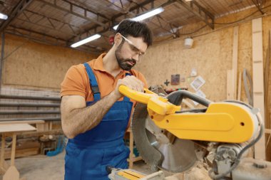Daire testere ile çalışan erkek marangoz atölyede zanaatkarlıktan zevk alıyor. Ahşap mobilya imalatı ustası için profesyonel ekipman.