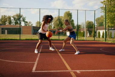İki kız basketbolcu top sürüyor açık hava sahasında rekabetin tadını çıkarıyorlar.