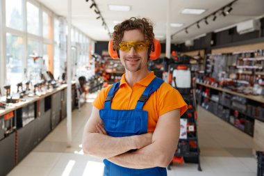 Endüstriyel işler için koruyucu vitesler takan gülümseyen adam portresi hırdavatçı dükkanının içinde duruyordu. Gürültü önleyici kulaklıklar ve güvenlik gözlüklerinin yeni gelişi