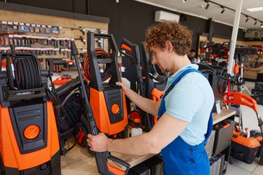 Hırdavatçıdan yüksek basınçlı çamaşır makinesini seçen bir işçi. Profesyonel taşınabilir elektrikli temizleyici satışta.