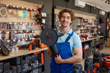 Hırdavatçıda büyük açılı değirmeni test eden bir işçi. Satılık endüstriyel elektrikli aletleri sergileyen mağaza asistanı