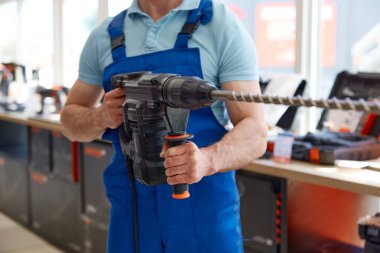 Elektrikli matkapla çalışan erkek işçi. Üniforma giyen erkek tamirci, satış için atölye ekipmanlarını kontrol ediyor.