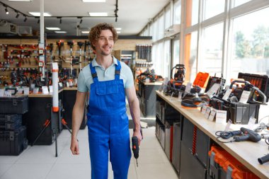 Tulum giyen işçiler hırdavatçıların vitrininde yeni matkaplarla yürüyorlar. İyi alışverişlerle tatmin oluyorlar.