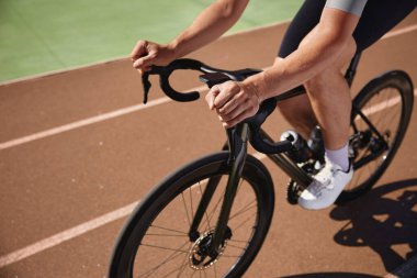 Direksiyonda el ele tutuşan bisikletçinin yakın görüntüsü. Sporcu tek başına velodromda pratik yapıyor. Aşırı hız sürüşünün keyfini çıkarıyor.