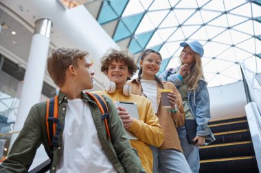 Alışveriş merkezinde yürüyen merdiven kullanan çok çeşitli gençlik grupları. Neşeli genç arkadaşlar dinleniyor. Olumlu yaşam tarzları, ergenlik anları.