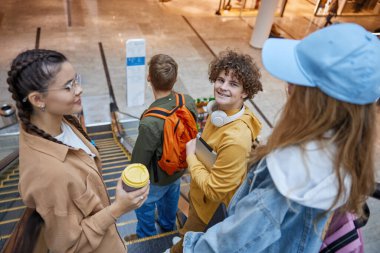 Alışveriş merkezinde yürüyen merdiven kullanan çok çeşitli gençlik grupları. Neşeli genç arkadaşlar dinleniyor. Olumlu yaşam tarzları, ergenlik anları.