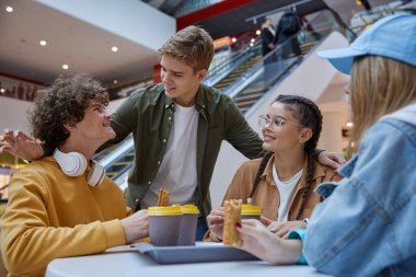 Genç arkadaşlar büyük şehir alışveriş merkezindeki kafede çerez yiyip kahve içiyorlar. Gençler hafta sonları toplanıp boş vakit geçiriyor.