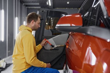 Araba yıkama servisinde çalışan usta bir adamın yan görüntüsü profesyonel deri temizleme ve tedavi prosedürü sağlıyor.