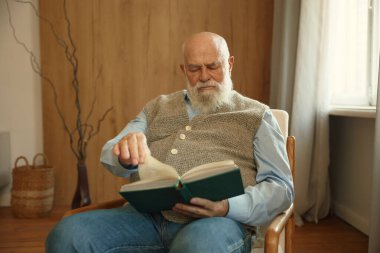Evdeki rahat koltukta oturup kağıt kitap okuyan ciddi emekli bir adam. Mutlu emeklilik, entelektüel hobi ve yaşlılar konsepti