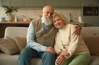 Oturma odasındaki kanepede oturan mutlu, yaşlı bir çiftin portresi. Yaşlılar uzun vadeli ilişki kavramını sever.
