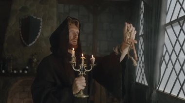 Bornozlu bir keşiş elinde gümüş haç tutarak dua ediyor. Pencerenin yanındaki manastırda tarihi bir rahip.