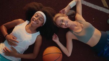 Mutlu, çekici, güler yüzlü genç spor kızları basketbol sahasında kameraya bakarak gülümsüyorlar.