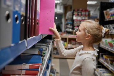 Güzel küçük kız kırtasiye dükkanından yeni kağıt arşiv klasörü seçiyor. Okul hazırlığı, perakende pazarından alışveriş.