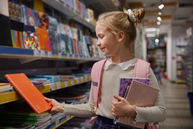 Kız öğrenci süpermarket kırtasiyesinde alışveriş yapıyor. Okulda okumak için kitap alan sevimli küçük kız modern dükkanda alışverişin keyfini çıkarıyor.