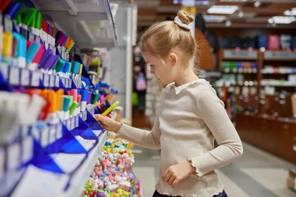 Küçük liseli kız modern kırtasiyede kalem seçiyor. Küçük bayan çocuk süpermarkette okul alışverişi yapıyor.