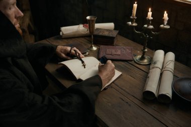 Ortaçağ keşiş tarihçisinin karanlık manastır hücresinde mum ışığı altında antik kutsal el yazması yazması.