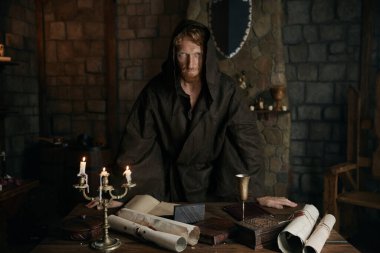 Ortaçağ taş manastırı duvarlarının eski masasında dururken mistik bir bakış açısıyla kameraya bakan başkeşiş ya da başrahibin portresi.