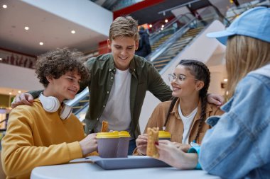 Gençler alışveriş merkezinin kafeteryasında dinleniyor. Genç adam arkadaşlarıyla takılıp eğlenmeye davet ediyor.