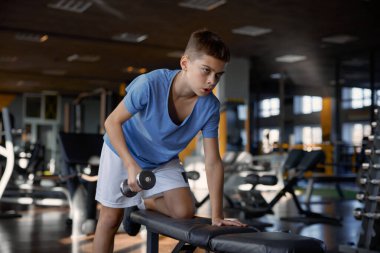 Zayıf vücut eğitimi almış, spor salonunda ilham almış genç bir çocuk. Genç halterci, halterleriyle pratik yapıyor. Hevesli bir şekilde kaslarını şişiriyor.