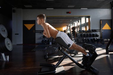 Genç çocuk spor salonunda özel spor malzemelerini kullanarak pres yapıyor. Genç sporcu kaslarını çalıştırarak kaslarını şişiriyor.