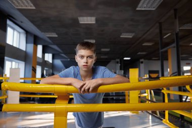 Modern spor salonundaki boks ringinde duran yorgun gencin portresi. Yakışıklı genç dövüşçü kameraya bakıyor. Çocuklar için kişisel eğitim fırsatı ve spor mücadelesi