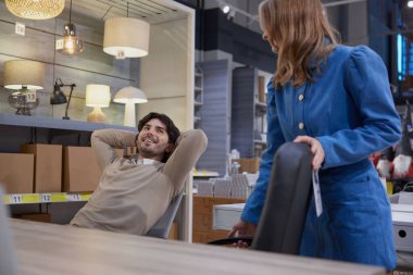 Birlikte mobilya mağazası keşfeden genç bir çift uygun bir sandalye seçiyor.