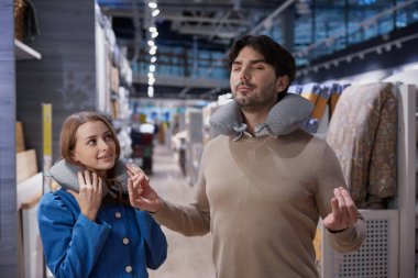 Modern perakende mağazasında kadın ve erkek birlikte boyun seyahat yastığını test ediyorlar.