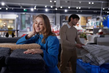 Neşeli ve mutlu bir kadın, rahat bir perakende satış ortamında çeşitli yumuşak havlular arasında neşe içinde poz verir.