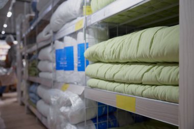 Perakende mağazasında çeşitli battaniye ve yastıklarla dolu uzun bir sıra düzenlenmiş raf.