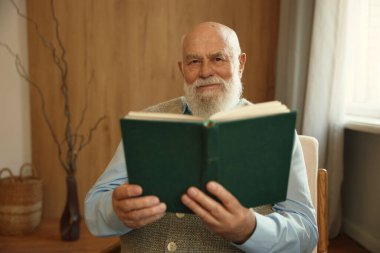 Evdeki rahat koltukta oturup kağıt kitap okuyan ciddi emekli bir adam. Mutlu emeklilik, entelektüel hobi ve yaşlılar konsepti