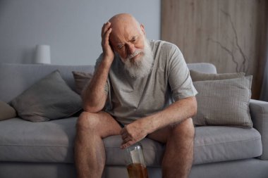 Oturma odasındaki kanepede tek başına içki içen üzgün son sınıf öğrencisi. İçki zararlı bir alışkanlık ve alkol bağımlılığı