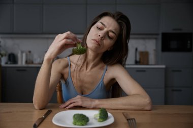 Tatmin olmamış anoreksik kadın evde brokoli yerken yüzünü buruşturuyor. Hayal kırıklığına uğramış genç bir kız elinde sebzeyle beslenme bozukluğu ve iştahsızlık çekiyor.
