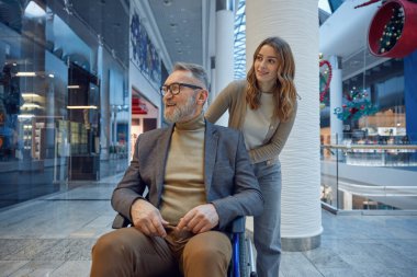 Güzel bir kadın, yumuşak ışıkla dolu uzun bir koridor boyunca tekerlekli sandalyedeki bir adamı nazikçe itiyor.