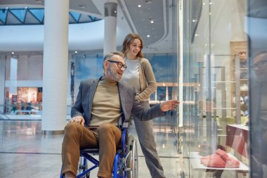 Tekerlekli sandalyedeki adam etrafındaki dükkanlar ve dükkanlarla dolu kalabalık bir alışveriş merkezinde geziniyor.