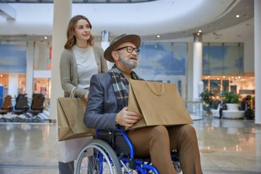 Tekerlekli sandalyede bir alışveriş merkezinde birlikte gezinirken kadınlardan yardım alan bir adam.