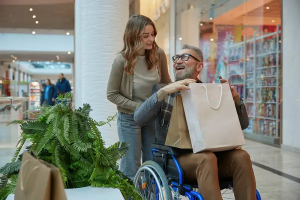 Tekerlekli sandalyede bir kadından yardım alan bir adam birlikte alışveriş merkezinde gezinirken...