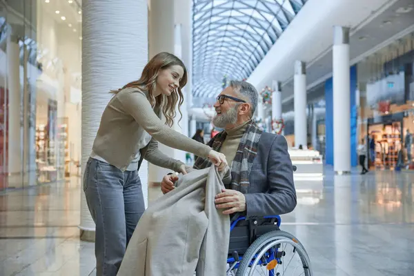 Bayan, tekerlekli sandalyedeki adamın üzerine yumuşak bir battaniye örterek onu sıcak ve rahat tutuyordu.