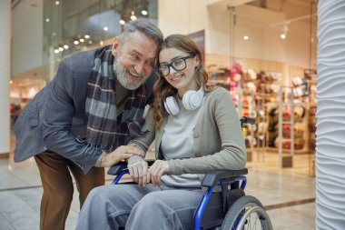 Neşeli bir büyükbaba ve tekerlekli sandalyedeki sevgili torunu canlı bir alışveriş merkezinde keyifli bir alışveriş deneyimini paylaşıyorlar.