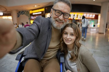 Genç bir kadın alışveriş merkezinde yaşlı bir adamla neşeli bir selfie çekerken neşeli bir etkileşim başlıyor.