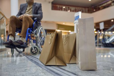 Alışveriş merkezinin içinde çanta ve tekerlekli sandalye kullanan bir adam alışveriş merkezinin çeşitli yönlerini keşfediyor.
