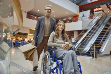 Tekerlekli sandalyedeki bir erkek ve kadın arasında hareketli bir alışveriş merkezinde güzel ve neşeli bir etkileşim başlar.