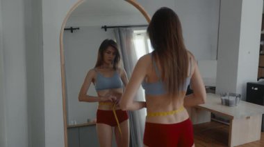 Sağlıksız anoreksik ince vücutlu kadın aynanın önünde belini ölçüyordu. Zayıflama saplantısı ve iştahsızlık çeken bir kadın.