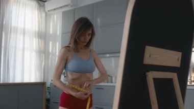 Sağlıksız anoreksik ince vücudu olan, aynanın önünde belini ölçen bir kadın. Zayıflama saplantısı ve iştahsızlık çeken bir kadın.