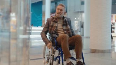 Tekerlekli sandalyedeki yaşlı bir adam alışveriş merkezinin vitrinine bakıyor.